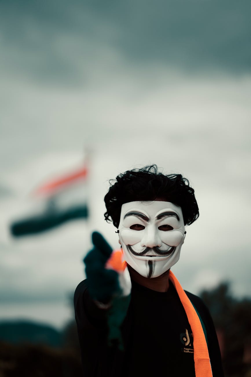 man in a guy fawkes mask with an indian flag in the background