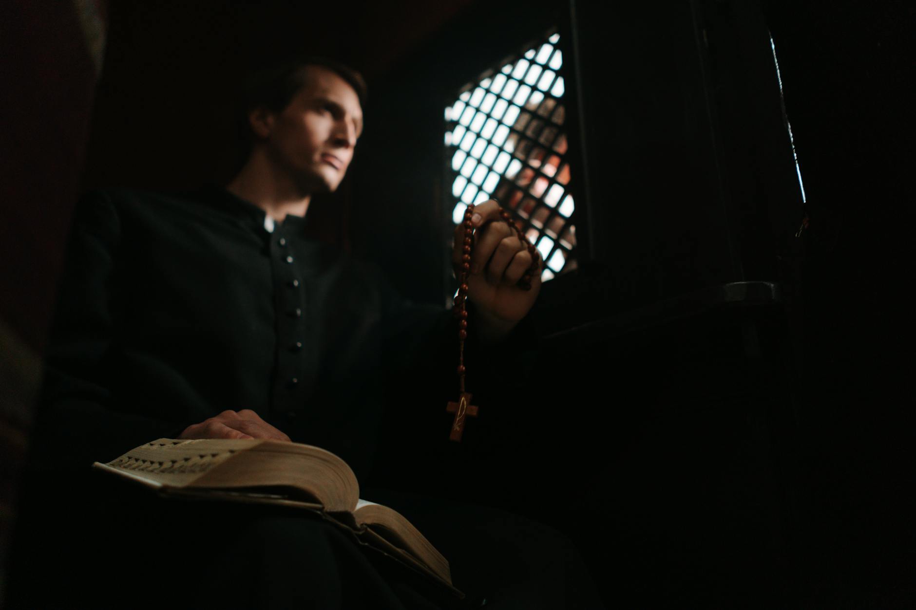 a low angle shot of a priest holding a bible and rosary